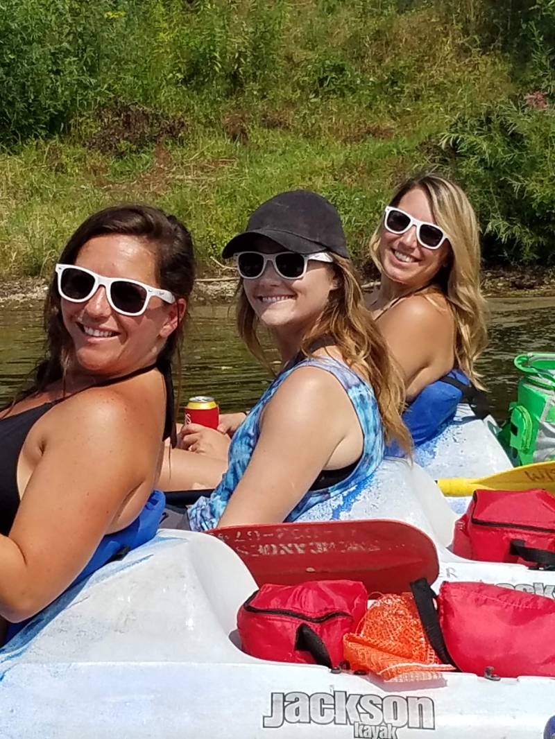 Three women in kayaks on a river, wearing sunglasses and holding drinks.