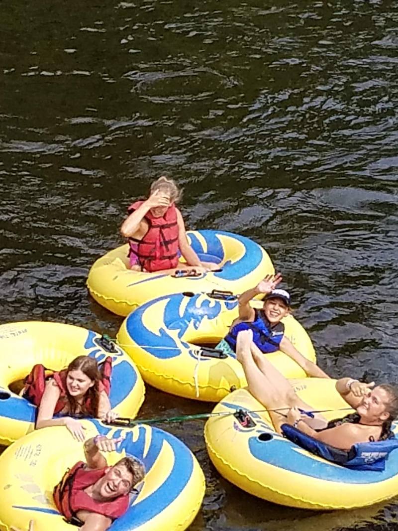 Group of people in yellow tubes floating on a river, smiling and waving.