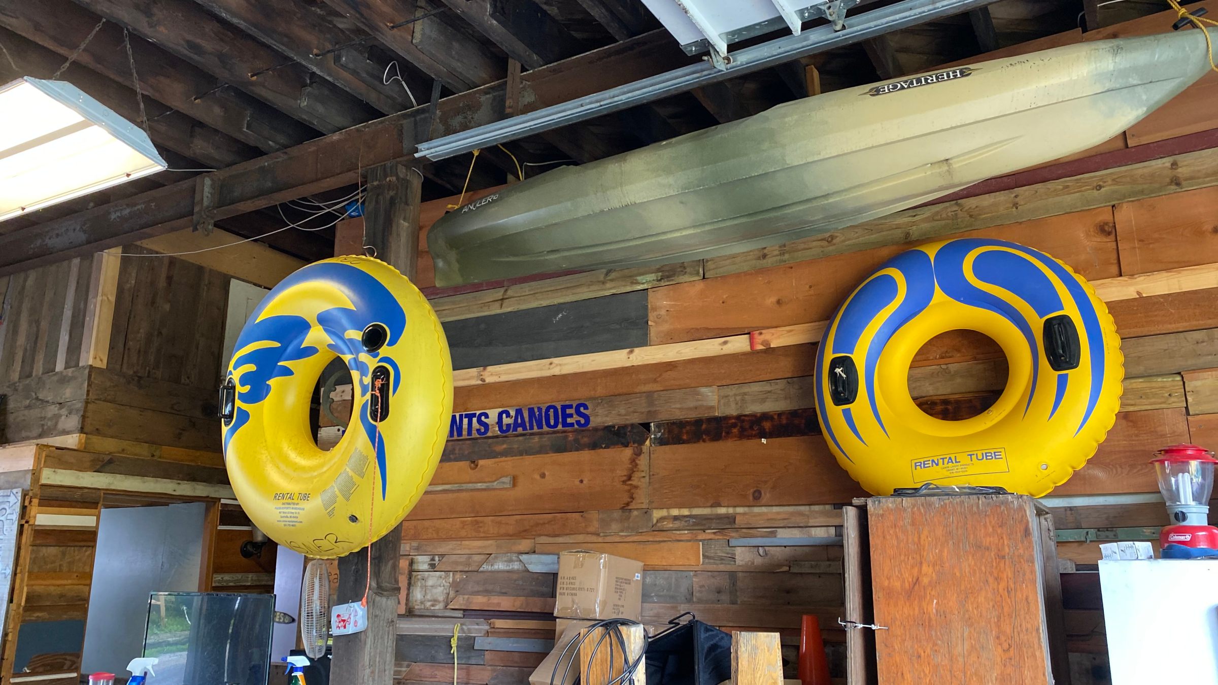 Two yellow and blue inflatable tubes and a canoe stored in a wooden garage.
