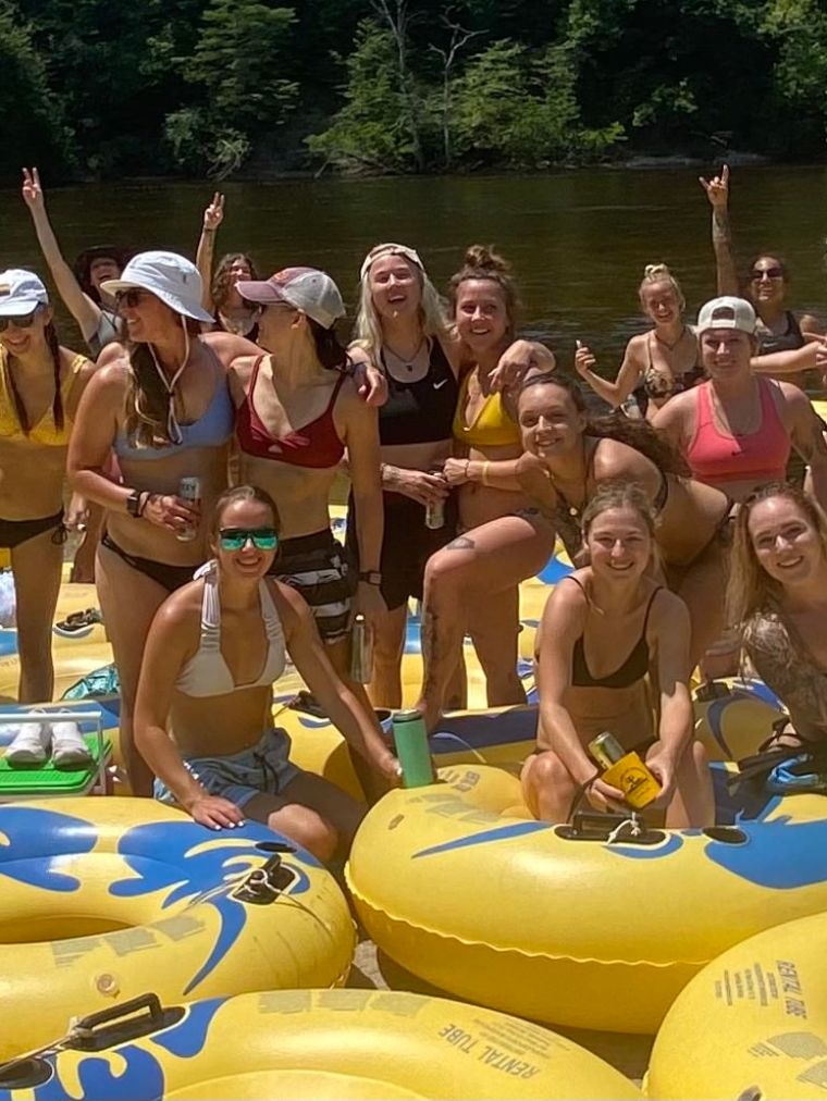 A group of people smiling on a riverside with yellow inflatable tubes.