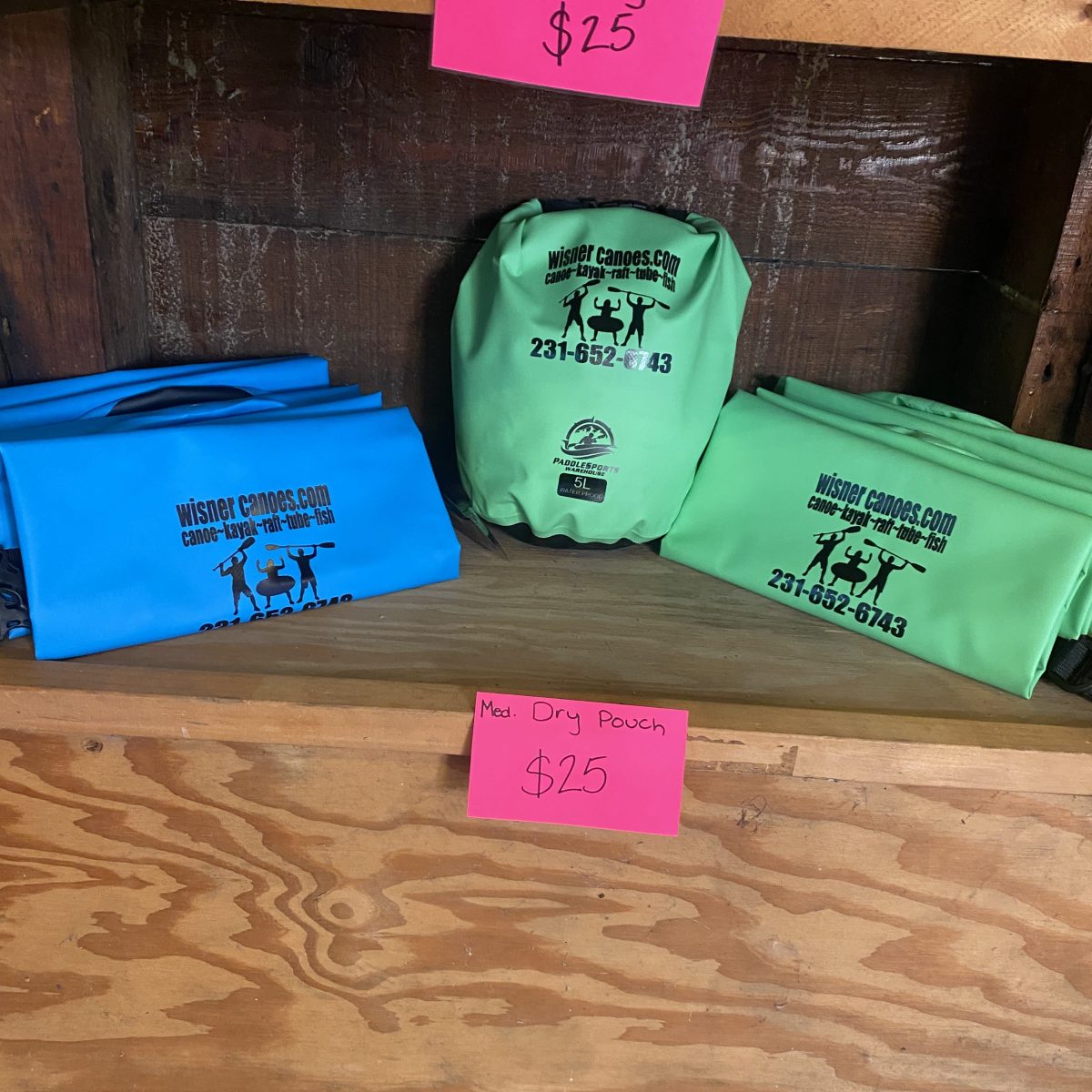 Blue and green dry bags displayed on shelves with pink price tags showing $25.