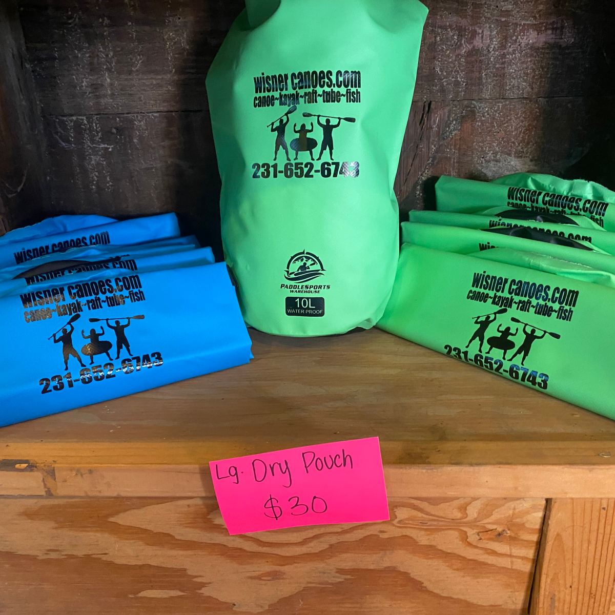 Green and blue waterproof pouches stacked on wooden shelf with $30 pink sign.