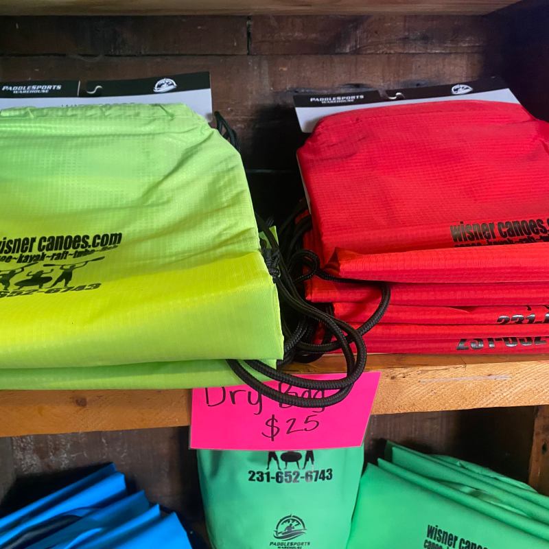 Colorful dry bags on shelf with 'wisner canoes' logo and pricing sign.