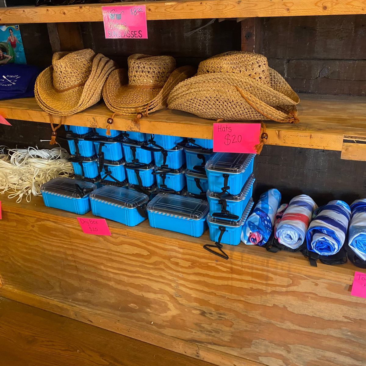 Store shelves with hats, blue boxes, ropes, and towels, each labeled with prices on pink signs.
