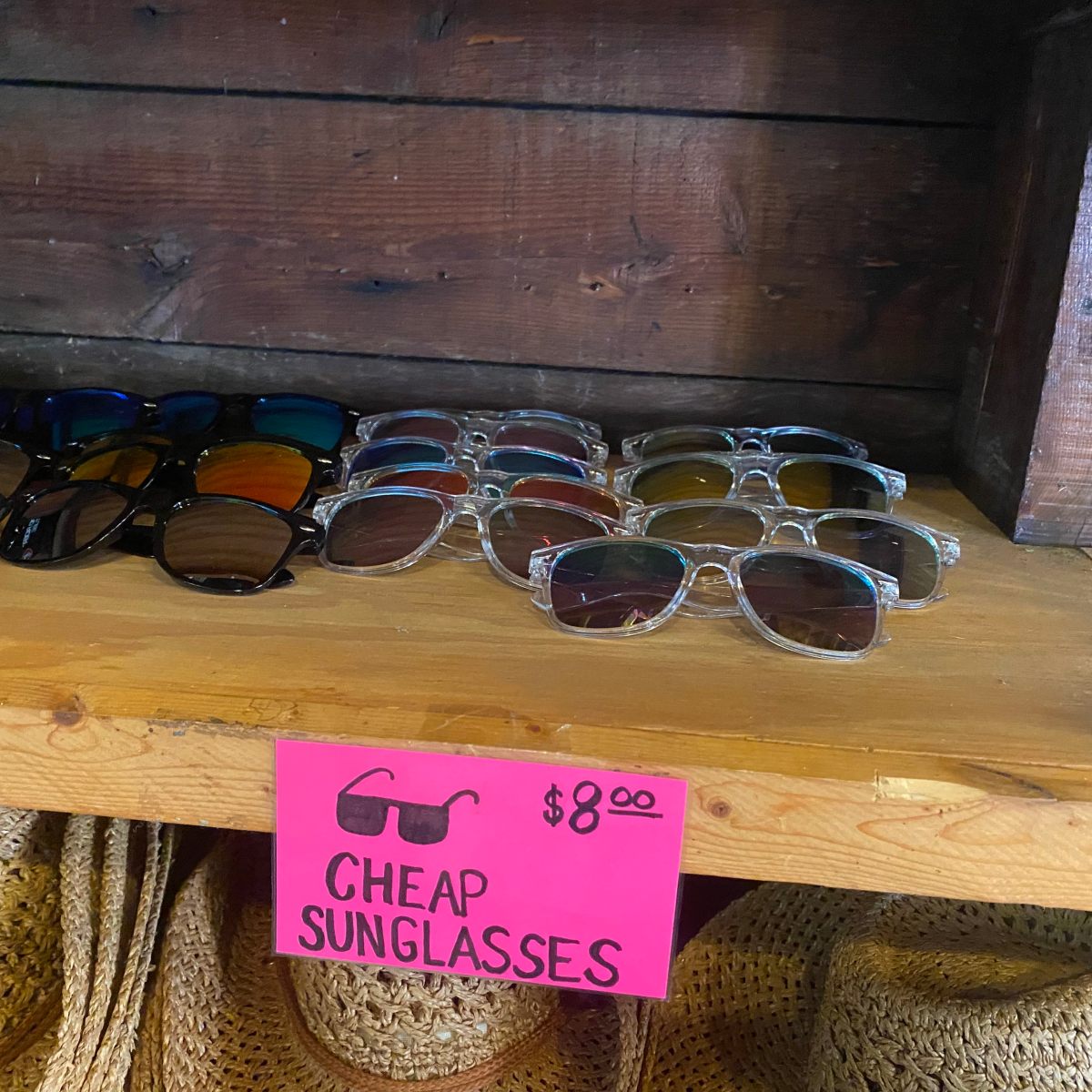 Various sunglasses displayed on a wooden shelf with a sign reading 'Cheap Sunglasses $8.00'.