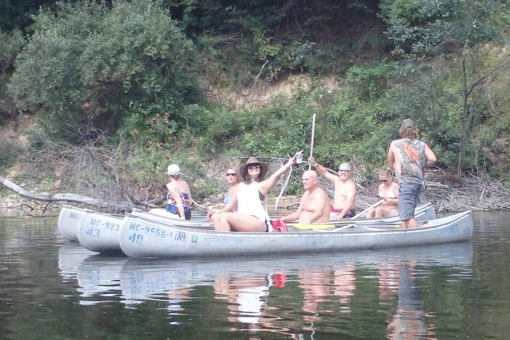 Group of people in canoes on a river, surrounded by lush greenery.