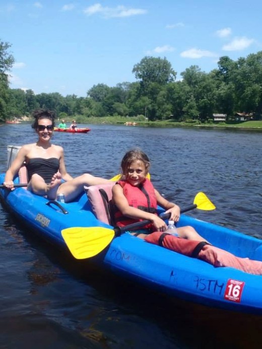 Two people kayaking on a river, surrounded by greenery on a sunny day.